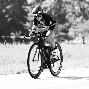 Dana Platin, endurance athlete, races on a bike with grass and trees in the background